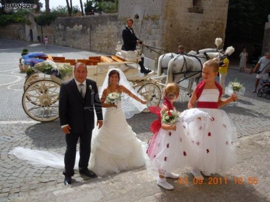 Gli sposi in posa fotografica con la carrozza con due cavalli bianchi sullo sfondo